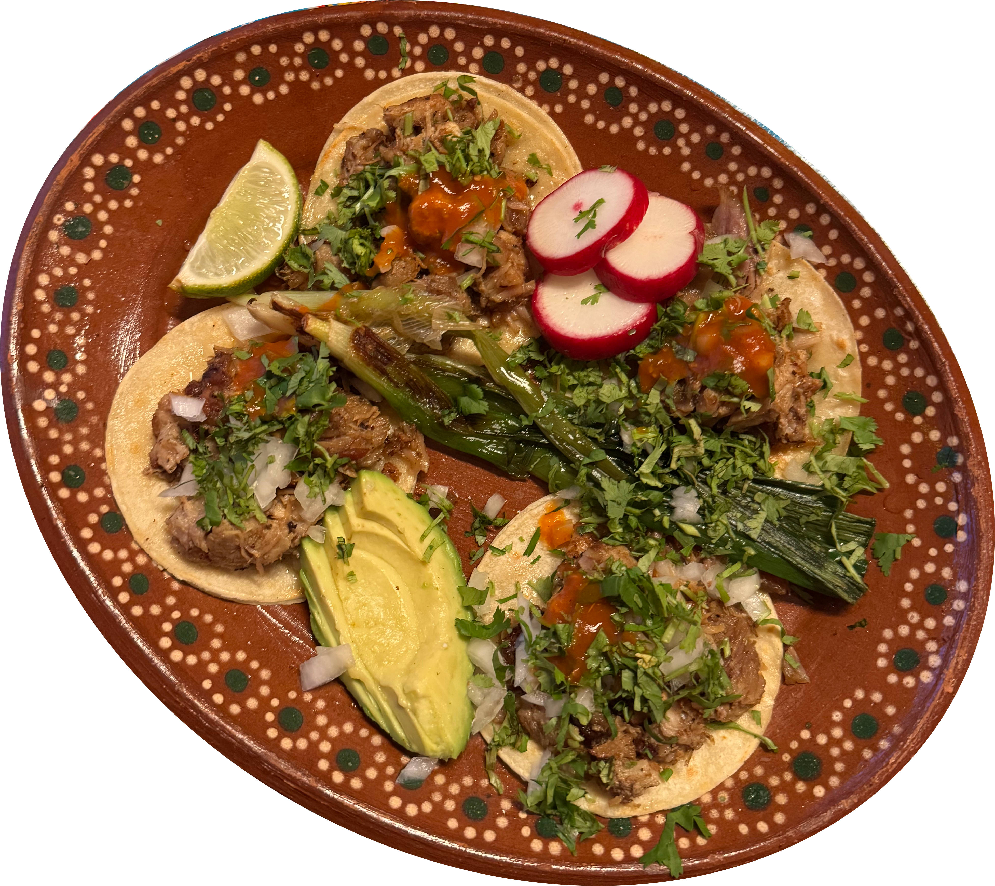 Four small carnitas tacos on a brown oval plate with a slide of avocado.